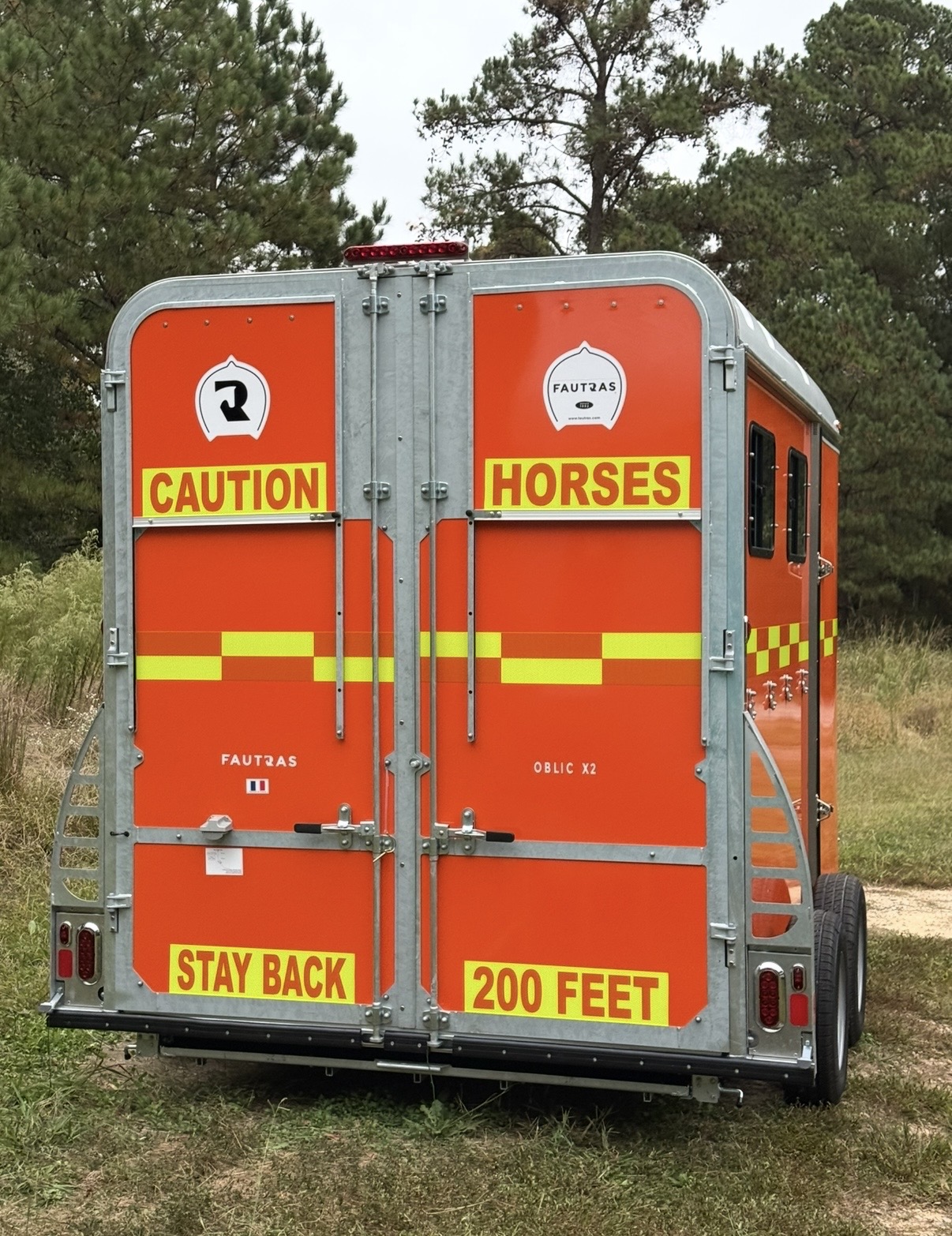 Orange Fautras horse trailer with fluorescent yellow reflective CAUTION HORSES and STAY BACK 200 FEET panels, plus chevron reflective tape strips for maximum rear visibility